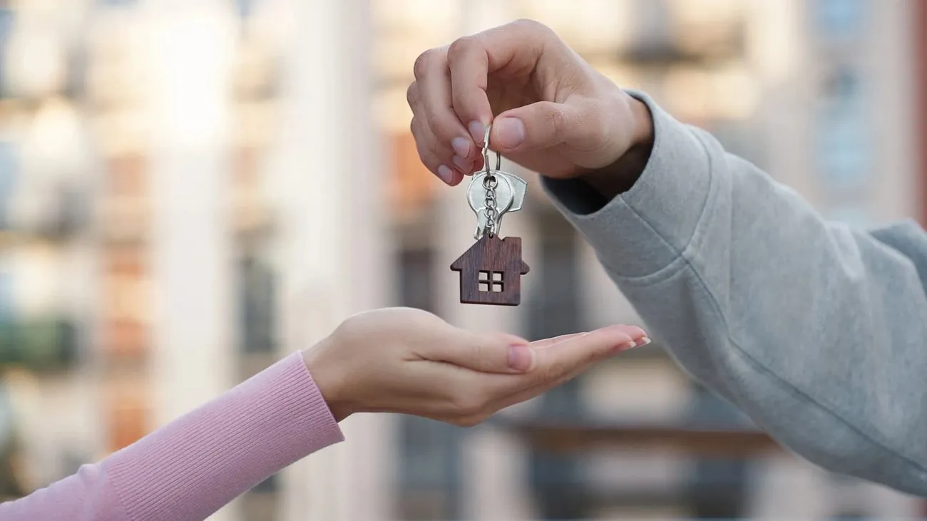 Hände halten ein kleines Haus mit Schlüssel